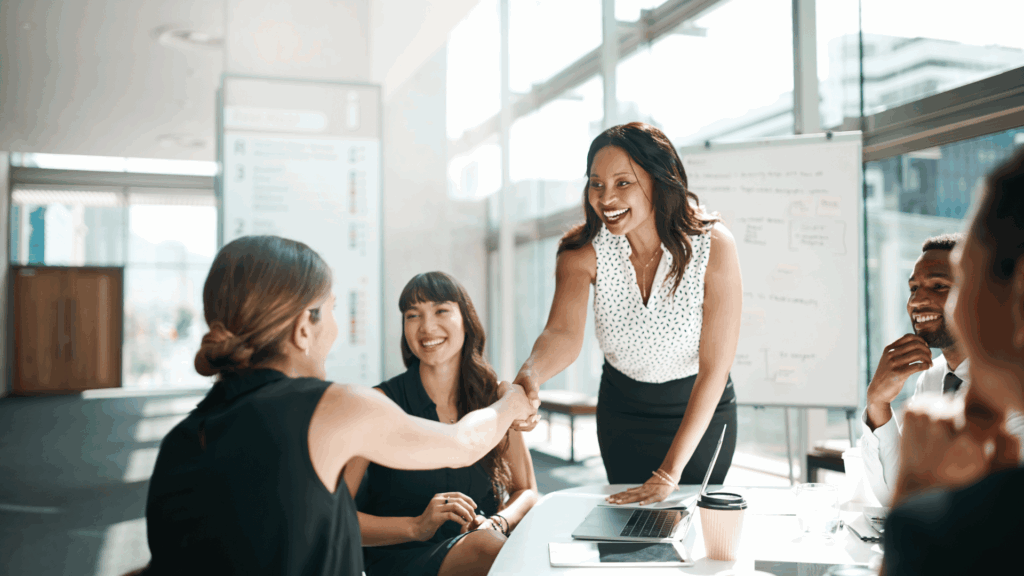 Two women shaking hands during a business meeting with other team members present