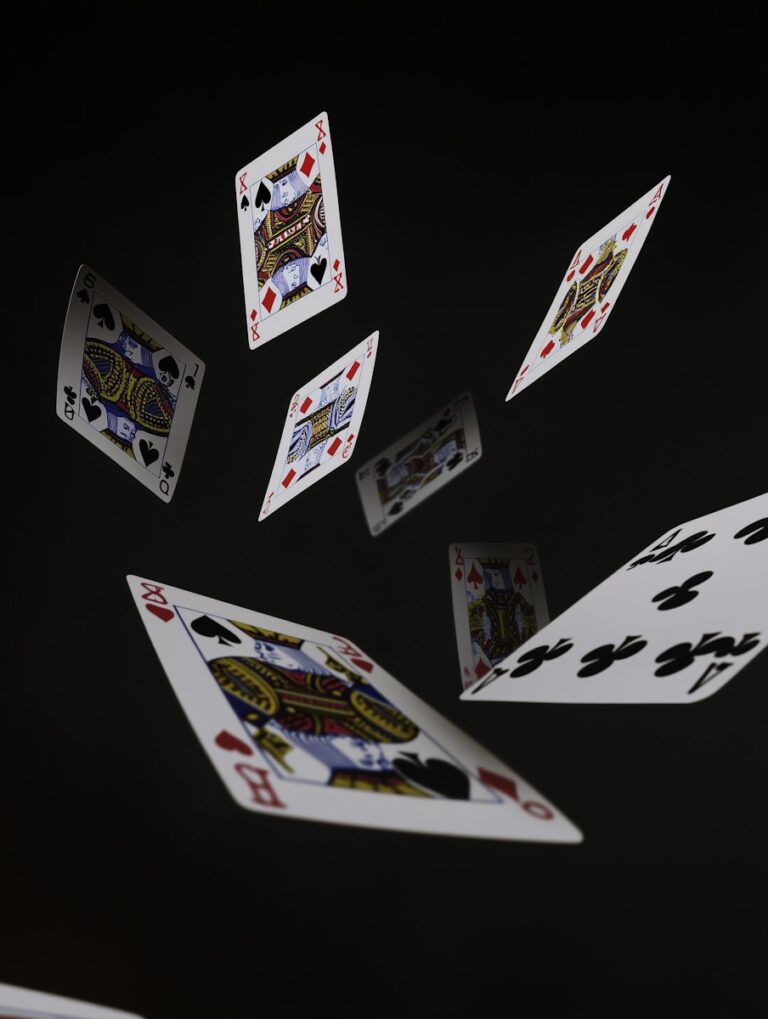 Photo showing several playing cards (Kings, Queens, and others) suspended in the air against a dark background.